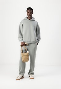 Lys grå hettegenser og joggebuksesett i et mykt stoff, kombinert med en liten lys beige crossover-veske. Skoene er hvite med brune såler.