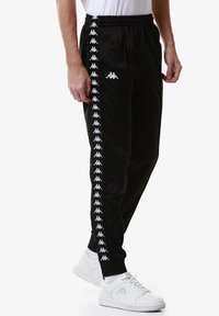 Pantaloni sportivi neri con una striscia logo bianca lungo i lati, realizzati in tessuto liscio con una vita elasticizzata e caviglie elasticizzate.