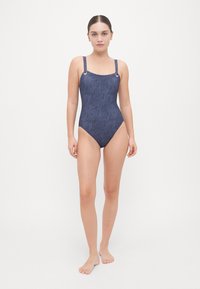 Marineblauwe badpak met een textuurpatroon, vierkante halslijn en verstelbare bandjes met zilveren hardware accenten.