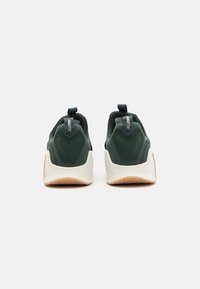 Nike-sko med en mørkegrøn overdel, hvid mellemsål og en gummigummi-ydersål. Hælen har et trækstrop og teksturerede designelementer.