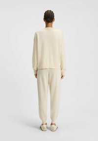 Cremefarbener Pullover und passende Jogginghose aus weichem Strickmaterial. Lässig geschnitten mit gerippten Säumen. Schlichte, neutrale Farbgestaltung und minimale Details.