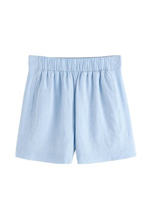 Kobieta ubrana w jasnoniebieskie szorty z wysokim stanem i kieszeniami, kwiecisty top od bikini oraz pasującą jasnoniebieską koszulę na plaży.