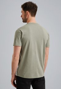 Camiseta de algodón verde oliva con mangas cortas, cuello redondo y un corte relajado. Costuras notables a lo largo del dobladillo y los bordes de las mangas.