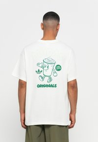 Witte katoenen t-shirt met een groene cartoonfiguur van een drankje en de tekst "ADIDAS ORIGINALS" en "ICED LATTE" op de achterkant.