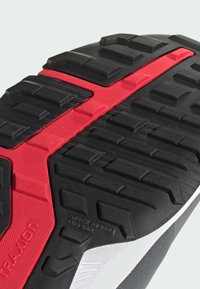 Suela de goma rugosa en negro y rojo con textura de zapatilla deportiva, con patrones de banda de rodadura profundos para una mejor tracción.