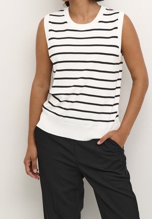 Sleeveless white top with black horizontal stripes worn with black pants; one hand in pocket, neutral background.