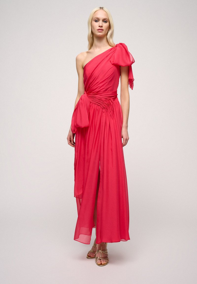 Asymmetrical one-shoulder dress in vibrant pink fabric. Features a ruched waist and flowing skirt, with a bow detail on the shoulder.