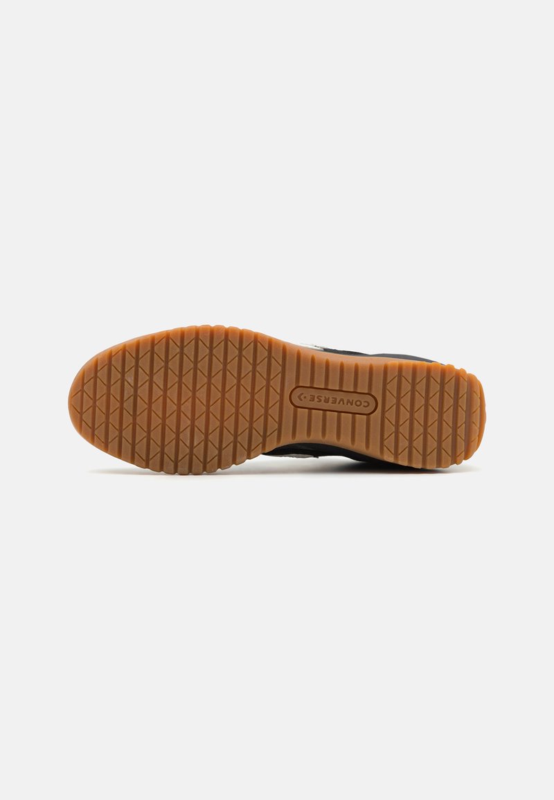 Suela de zapatilla negra con un patrón texturizado, que cuenta con una suela de goma color caramelo y el logotipo de "Converse" en el centro.