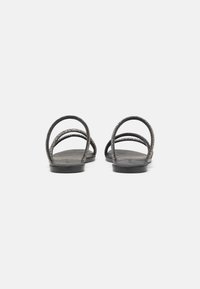 Des sandales plates noires avec trois fines lanières scintillantes et une semelle simple, vues de l'arrière sur un fond blanc.