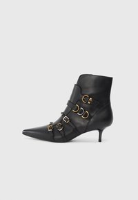 Botín de cuero negro hasta el tobillo con punta afilada, que presenta acentos de metal dorado y plateado, correas ajustables y un tacón modesto.
