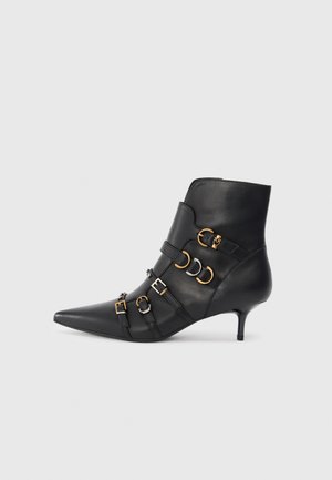 Black leather ankle boot with pointed toe, featuring gold and silver hardware accents, adjustable straps, and a modest heel.