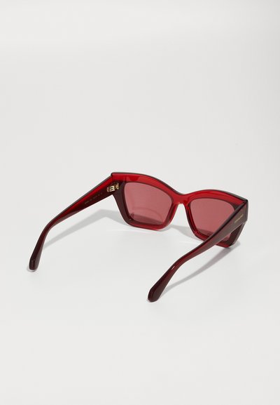 Gafas de sol rojas con un audaz diseño geométrico, que presentan un marco semitransparente y lentes ahumados. Acento de hardware dorado en la patilla.