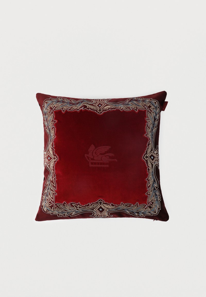 Coussin carré en velours rouge profond avec bordure brodée ornée et motif subtil de lion ailé au centre.
