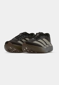 Μαύρα αθλητικά παπούτσια με ανοιχτόγριμες ρίγες, υφασμένο επάνω μέρος, μαλακή σόλα και ιδιαίτερο σχέδιο πέλματος στην εξωτερική σόλα.