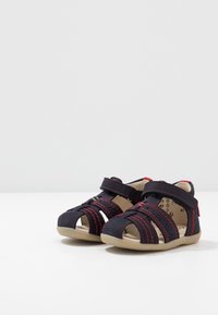 Sandalias para niños de color azul marino, fabricadas con un material suave, con costuras rojas, diseño de punta cerrada y correas ajustables.