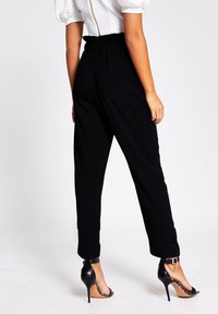 Black tapered trousers with a high elastic waistband, cuffed hems, and paired with black stiletto heels. Smooth texture, modern design.