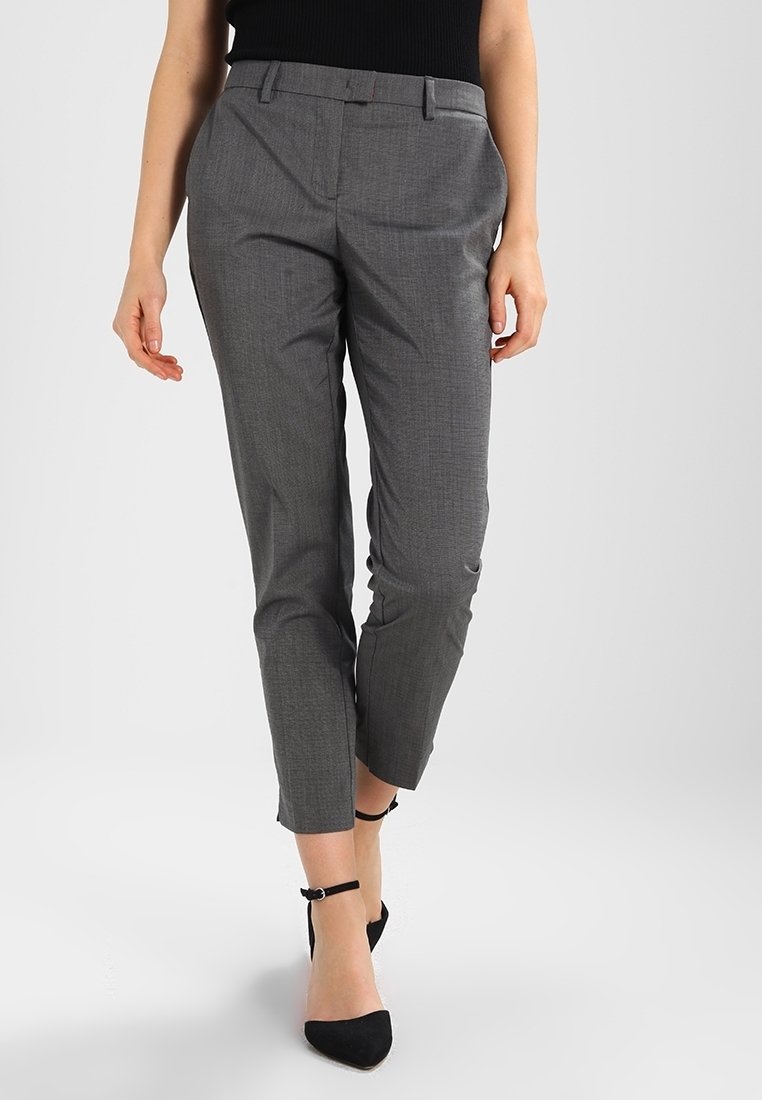 Pantalons gris ajustés avec une coupe slim, texture lisse et motif à carreaux subtil ; associés à des escarpins noirs à bride de cheville.