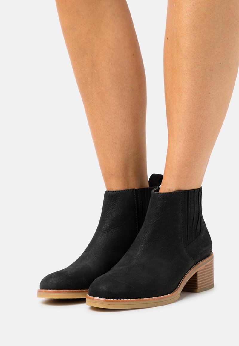 Bottines en suède noir avec panneaux latéraux élastiques, bouts ronds et un talon en bois empilé. Couture visible le long de la semelle.