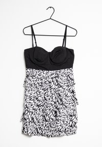 Abito in bianco e nero con top aderente caratterizzato da coppe sagomate, spalline sottili e una gonna a strati con rouches e motivi a foglia.