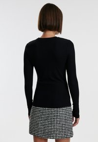 Zwarte ribbed top met lange mouwen in combinatie met een rokken met houndstooth-patroon. De stof is glad en heeft een aansluitende pasvorm.