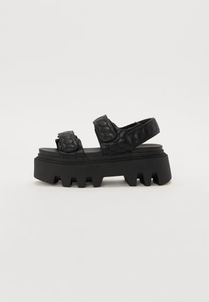 Black platform sandals with a textured upper featuring a hexagonal pattern, and a thick, ridged sole for traction.