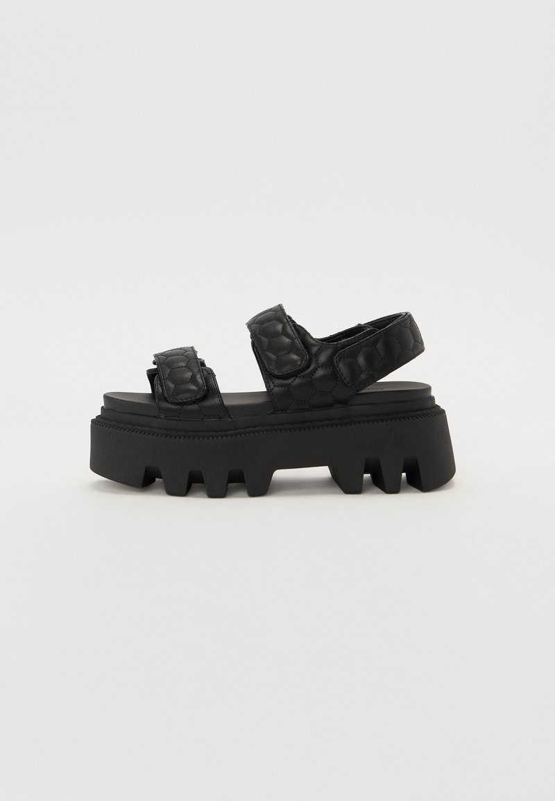 Black platform sandals with a textured upper featuring a hexagonal pattern, and a thick, ridged sole for traction.