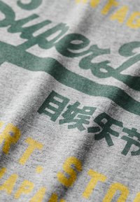 Tela de algodón gris con texto variado en verde y amarillo, con una apariencia texturizada. Los diseños incluyen caracteres japoneses y frases en inglés.