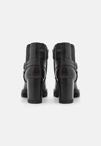 Botas de tobillo de cuero negro con tacón cuadrado, que cuentan con cremalleras laterales y correas decorativas. Textura lisa con detalles de costura.