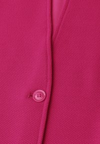 Tissu texturé rose vif avec un bouton rond assorti cousu près d'une couture verticale.