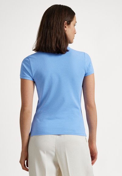 Svetlo modra polo majica s kratkimi rokavi iz mehke tkanine, z oprijetim krojem in rebrastim ovratnikom, oblečena z bež hlačami.