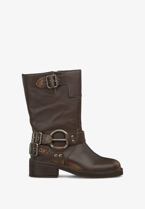 Botín de cuero marrón hasta el tobillo con punta redondeada, hebillas decorativas y un tacón grueso. Presenta una correa ajustable alrededor del tobillo.