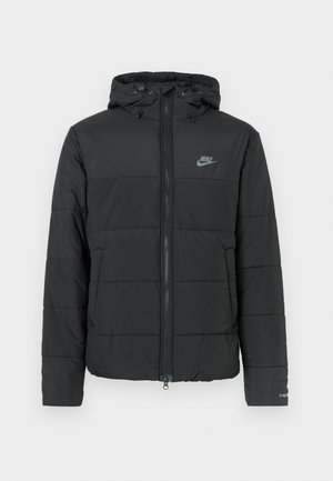 Černá péřová bunda s kapucí, má přední zip, horizontálně prošívaný vzor a malé logo na levé horní straně.