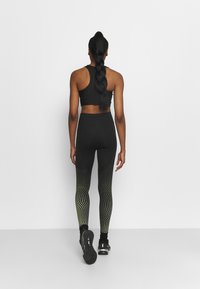 Czarny sportowy top w stylu crop i leginsy z wysokim stanem w gradientowy, kropek wzór, przechodzący od jednolitej czerni do żółtych akcentów. Czarne sneakersy.