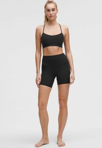 Conjunto deportivo negro que incluye un sujetador deportivo ajustado con tirantes finos y shorts de cintura alta, ambos fabricados en un tejido liso y elástico.