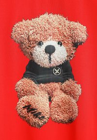 Diseño de camiseta con un oso de peluche de pelaje marrón, suéter negro y un logo, sobre un fondo rojo.