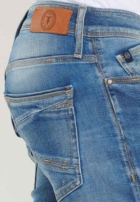 Lichtblauwe denim jeans met een tan leren patch op de taille, contrasterende stiksels en meerdere zakken met een lichte vervaging.