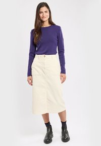 Lila langärmliges Oberteil kombiniert mit einem cremefarbenen Kord Midi-Rock, der seitliche Taschen und einen vorderen Knopfverschluss hat, getragen mit schwarzen Stiefeln.