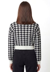 Cropped trui in zwart-wit pied-de-poule patroon, met geribbelde zoom en manchetten, gemaakt van een zacht gebreid materiaal.
