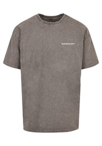 T-shirt grigio a maniche corte con una texture leggermente sbiadita. Ha un collo a giro e un piccolo logo bianco sul davanti. Forma quadrata.