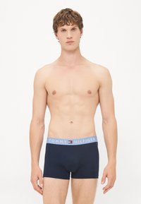 Marineblaue Boxerbriefs mit einem hellblauen elastischen Taillenbund, der das Logo "TOMMY HILFIGER" trägt. Baumwollmaterial mit einer glatten Textur.