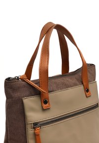 Rudas audinio rankinė su dviem rudais odiniais rankenomis, smėlio spalvos priekinis skydelis ir užtraukiama kišenė. Patvarios medžiagos su kontrastinėmis tekstūromis.