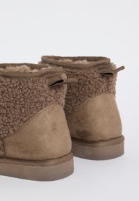 Braune Knöchelstiefel mit einem weichen Fleece-Obermaterial, Wildlederakzenten und doppelten Schlaufen-Anziehhilfen. Flache Gummisohlen sorgen für Komfort und Stabilität.