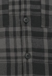 Close-up of black and gray checkered fabric with two black four-hole buttons and visible stitching along the seams.