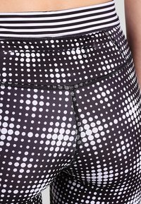 Leggings neri con un motivo a pois composto da cerchi bianchi di varie dimensioni. La vita presenta strisce orizzontali bianche e nere.