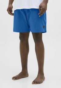Blauwe zwembroek gemaakt van lichtgewicht stof, met een elastische tailleband, een gladde textuur en een klein zwart logo-label aan de zijkant.