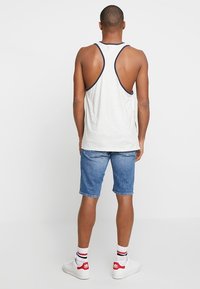 Šedý top bez rukávů s námořnickým lemem a otevřeným zadním dílem, spárovaný s denimovými šortkami. Bílí tenisky a pruhované ponožky dotvářejí celkový vzhled.