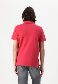 Polo rouge avec un col et des manches courtes, présentant une texture lisse. La chemise est associée à un short en denim gris.