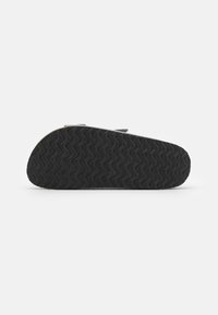 Semelle de chaussure en caoutchouc noire avec un motif ondulé texturé, présentant une légère courbure à l'avant et une construction robuste pour une meilleure adhérence.