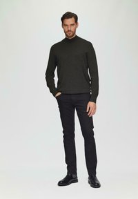 Donkere trui met hoge kraag, gecombineerd met zwarte slim-fit jeans en zwarte ronde schoenen. Glad textuur en minimalistisch ontwerp.