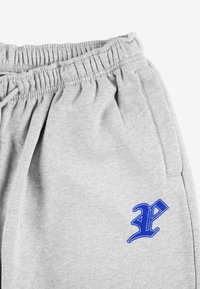 Szare spodnie dresowe z elastycznym pasem, z niebieskim haftowanym logo po lewej stronie oraz miękkim, teksturowanym materiałem.